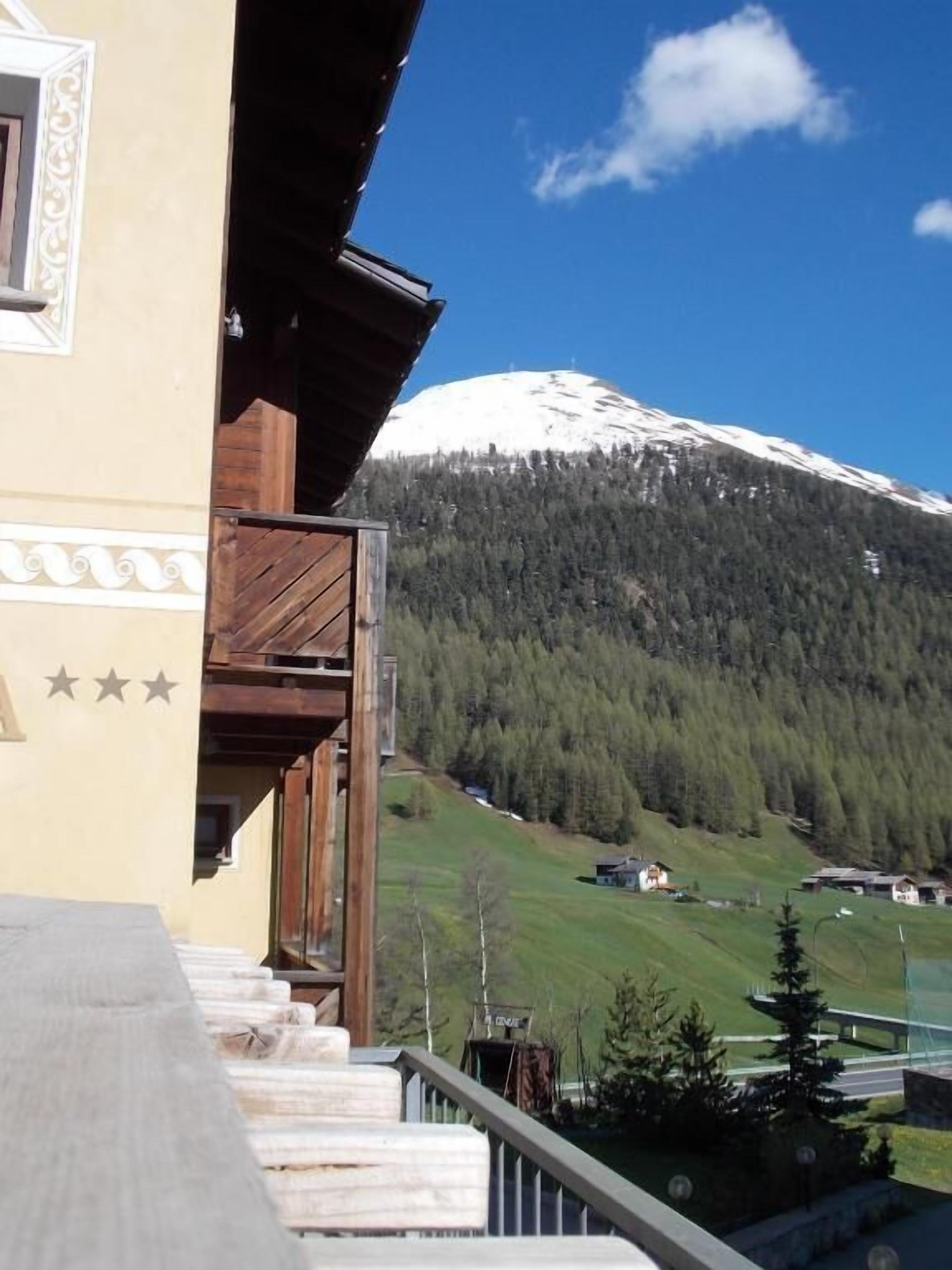 Ein Berg mit schneebedeckter Spitze, ein bewaldeter Hang und ein Gebäude mit einem Balkon mit Blick auf die Landschaft.