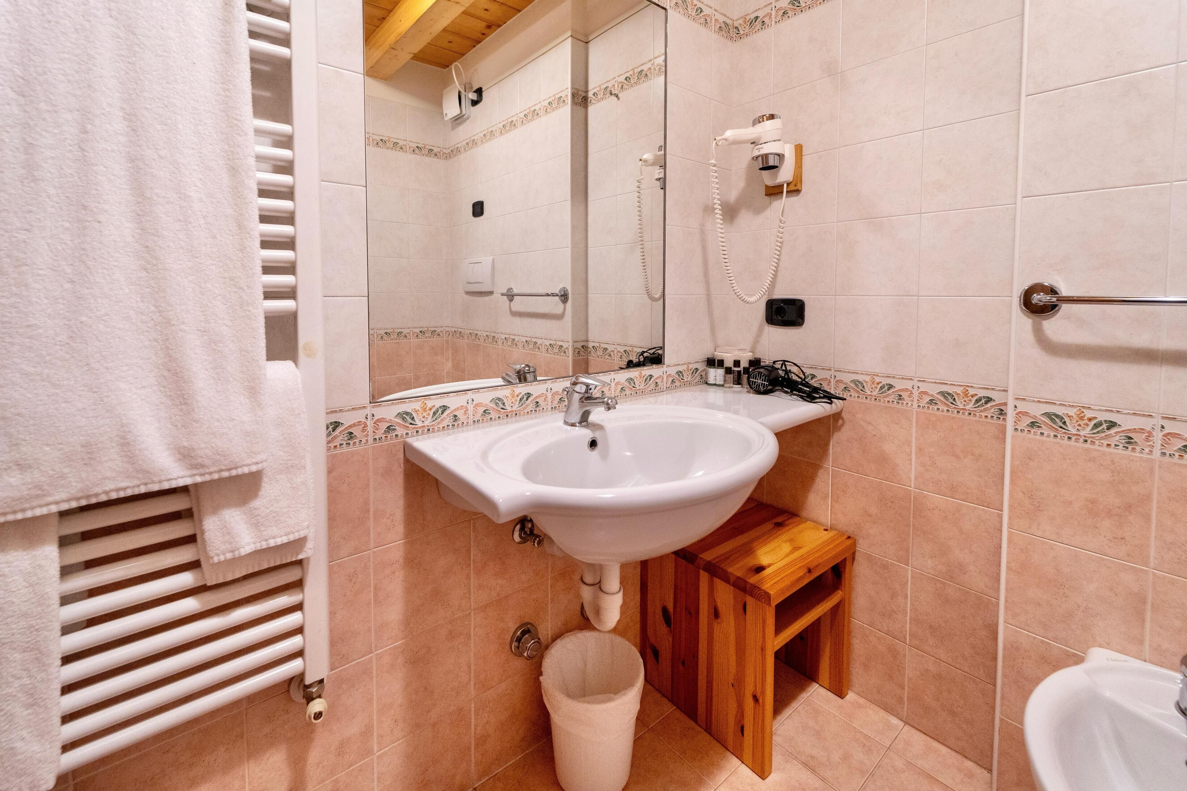 Un baño con lavamanos, espejo, perchero para toallas y un pequeño taburete de madera.