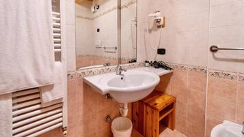 Un baño con lavamanos, espejo, perchero para toallas y un pequeño taburete de madera.