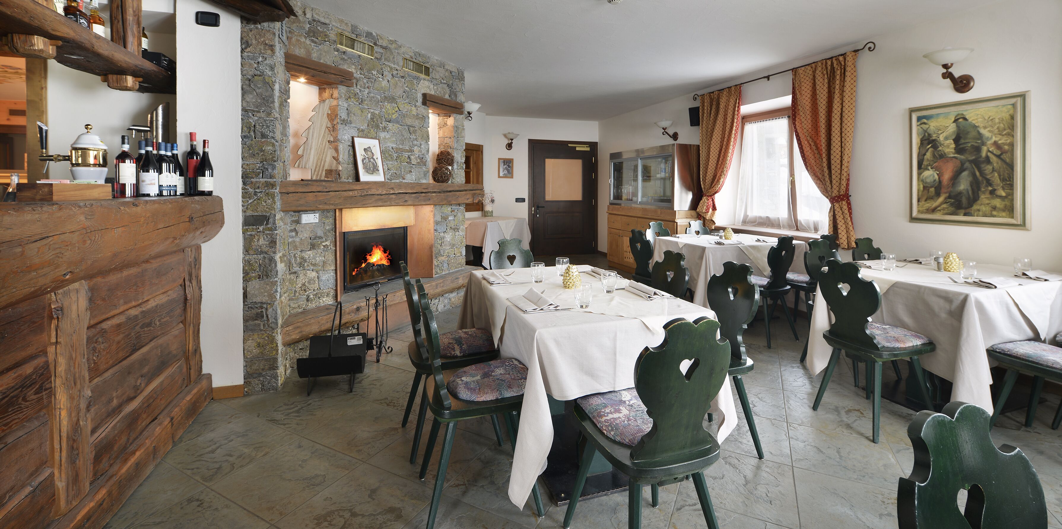 Uma sala de jantar com lareira de pedra, balcão de madeira e várias mesas preparadas para refeições.