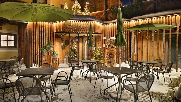 An outdoor dining area with tables and chairs, covered by umbrellas, and decorated with Christmas trees. - Hotel Primula (Livigno)