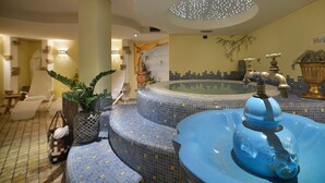 A luxurious bathroom with a large bathtub, a whirlpool, and a seating area with a chair and a plant. - Hotel Primula (Livigno)