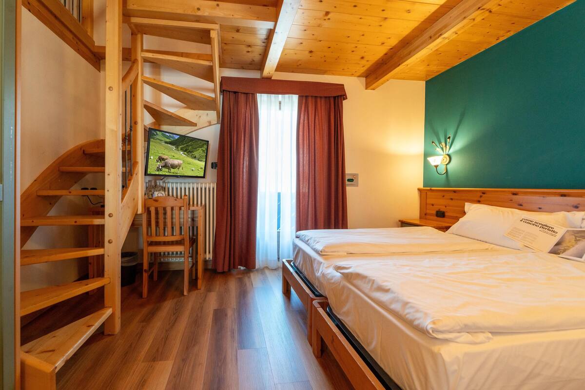 Un escalier en bois menant à une mezzanine aménagée avec un lit et un bureau.