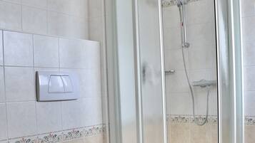 A bathroom with a glass-enclosed shower, a toilet, and a sink.