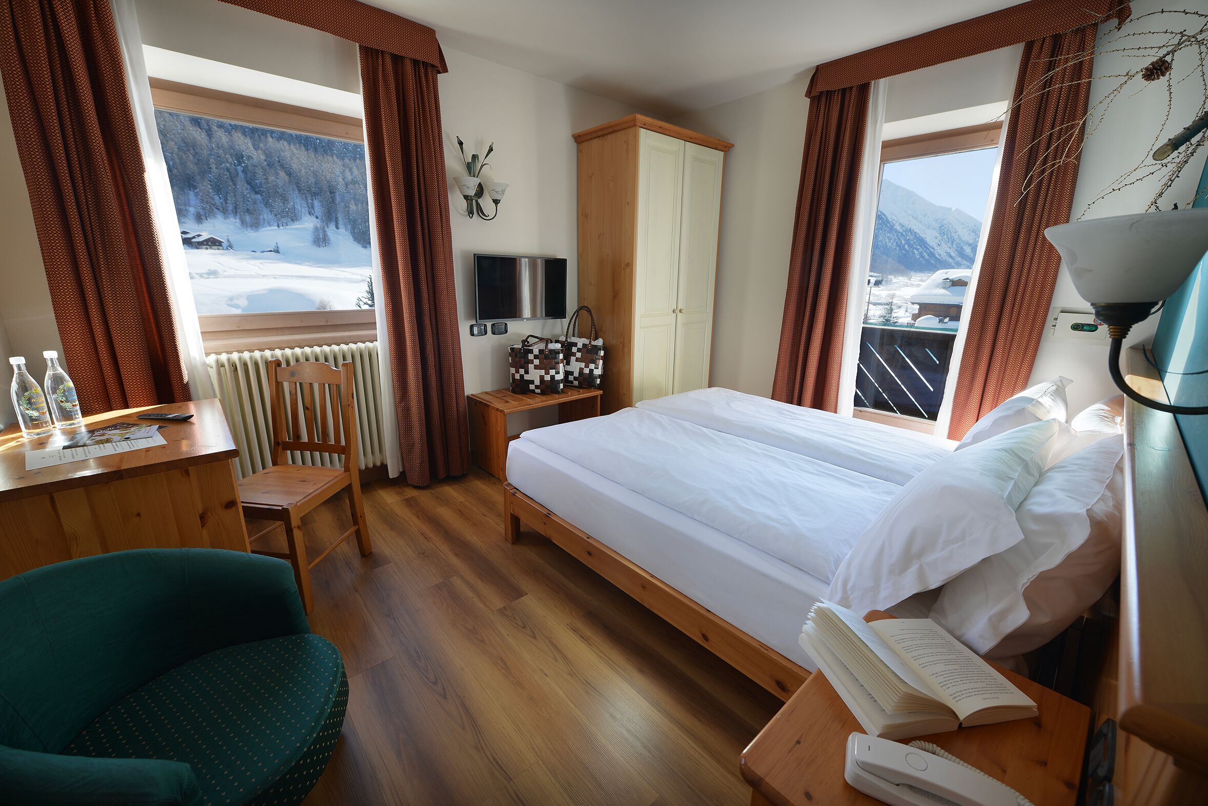 Ein Hotelzimmer mit Bett, Schreibtisch mit Stuhl, Kleiderschrank, Fernseher und Blick auf eine verschneite Landschaft.