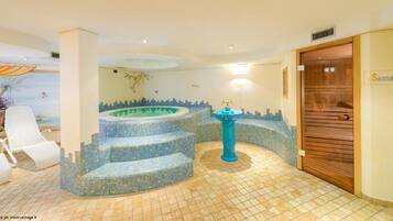 Ein Wellnessbereich mit einem blauen Mosaikpool, einer hölzernen Sauna-Tür und einem gefliesten Boden.