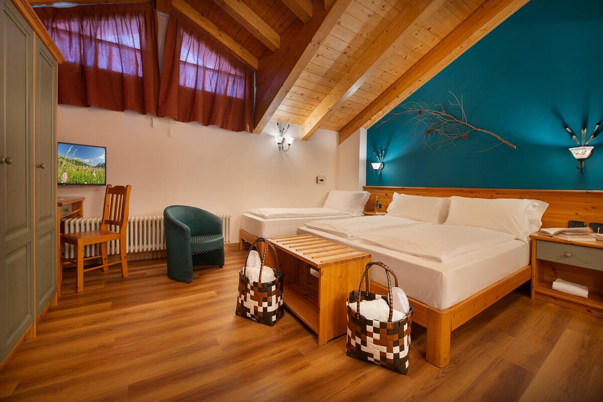 Une chambre avec un plafond en bois, deux lits, une table de chevet en bois, une chaise, une petite table et une vue sur un paysage par la fenêtre.