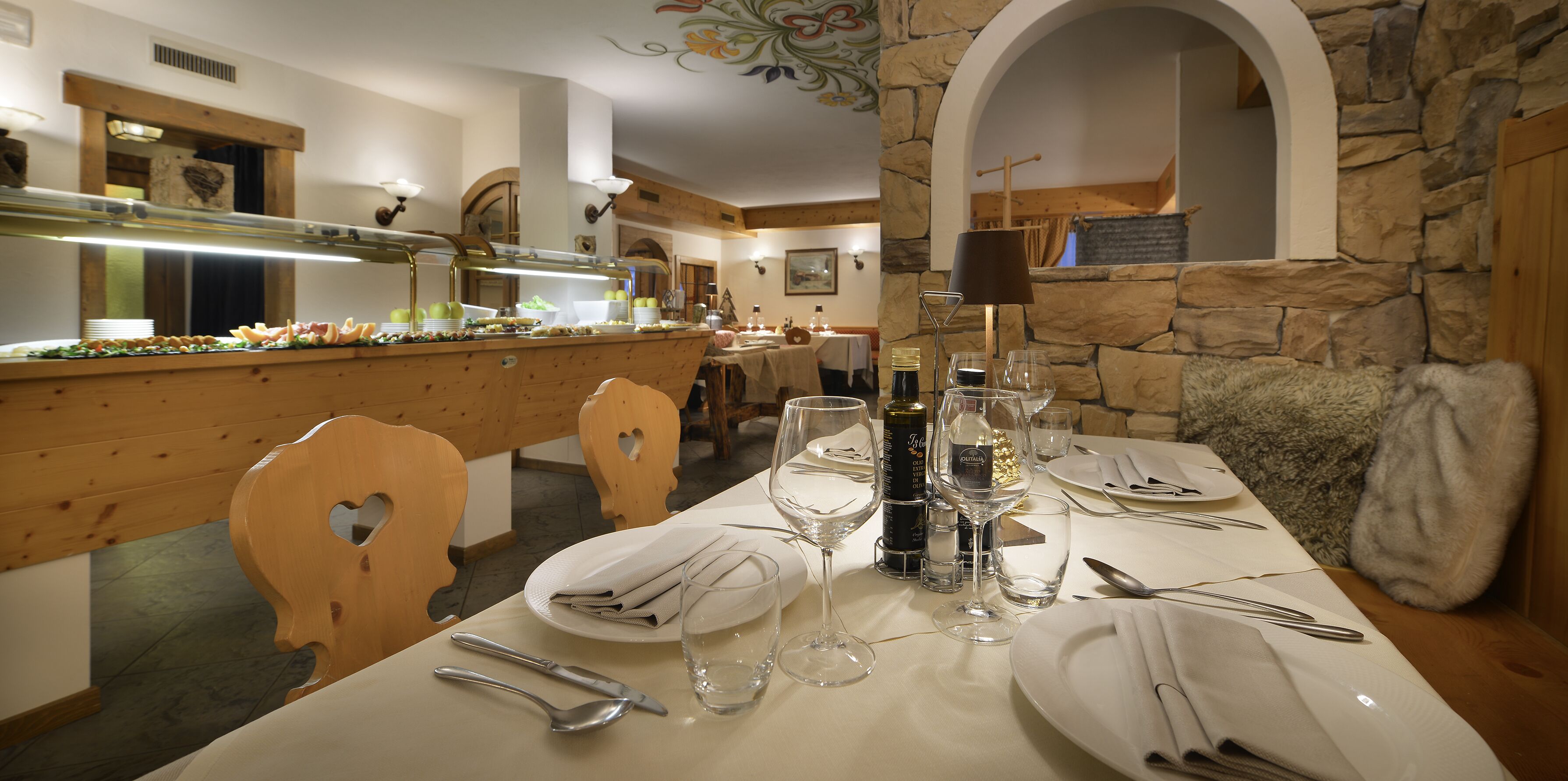 A dining area with a buffet setup, wooden chairs, a stone wall, and a chandelier.