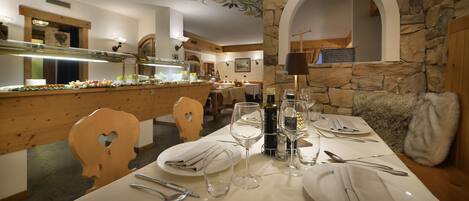 A dining area with a buffet setup, wooden chairs, a stone wall, and a chandelier.