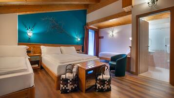 Habitación de hotel con pisos de madera, una cama grande, dos mesitas de noche, un buró de madera, una lámpara de pared, una pequeña mesa de madera, dos cestas tejidas y vistas al baño a través de una puerta abierta.