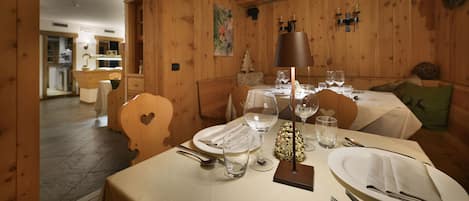 Een eethoek met houten wanden, een stoel in hartvorm en een tafel gedekt met witte tafelkleden, bestek en wijnglazen.