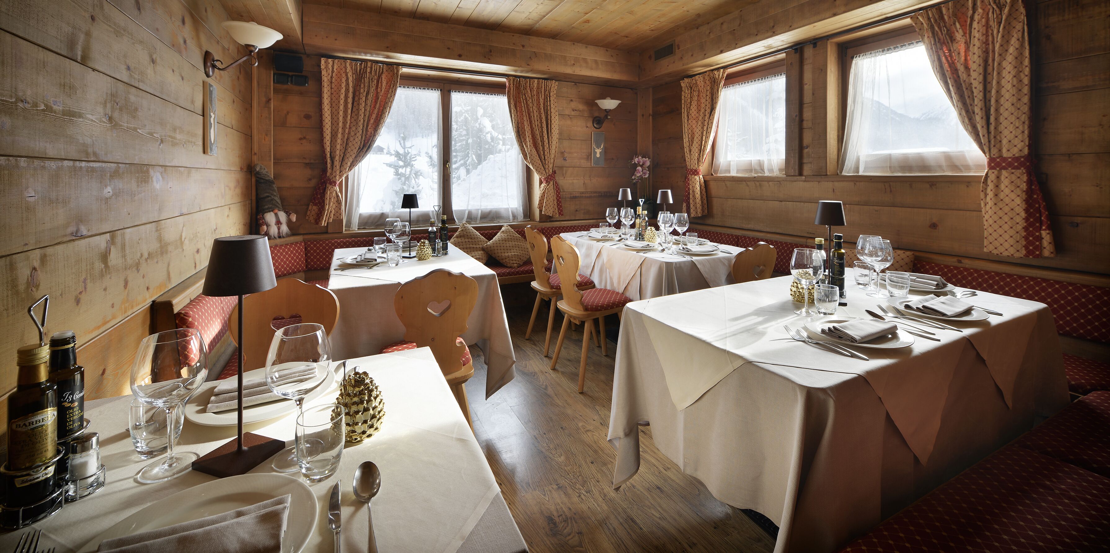 Una cabaña de madera acogedora con comedor que tiene mesas dispuestas para dos, bancos de madera y un ventanal con cortinas.