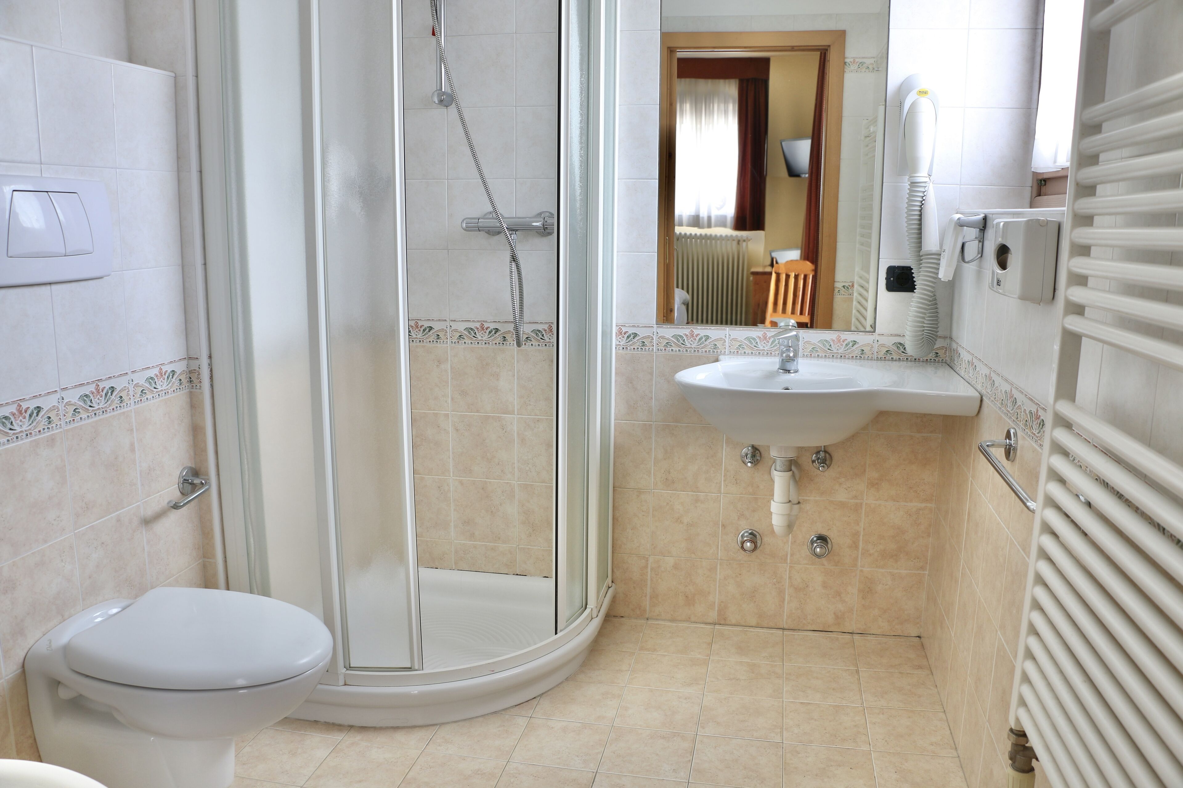 A bathroom with a toilet, a shower with a glass door, a sink, and a radiator.