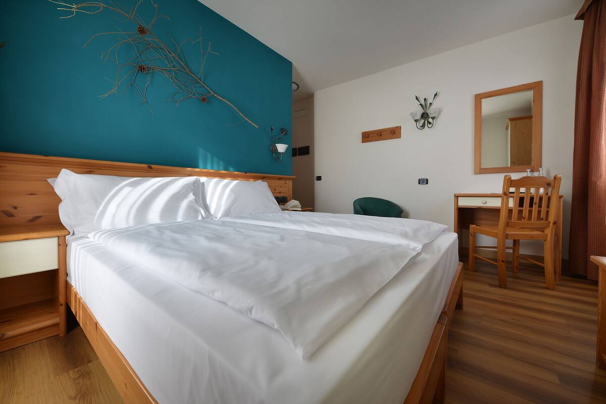 Un lit bien fait, avec du linge de lit blanc, une tête de lit en bois et un mur d’accent de couleur turquoise.