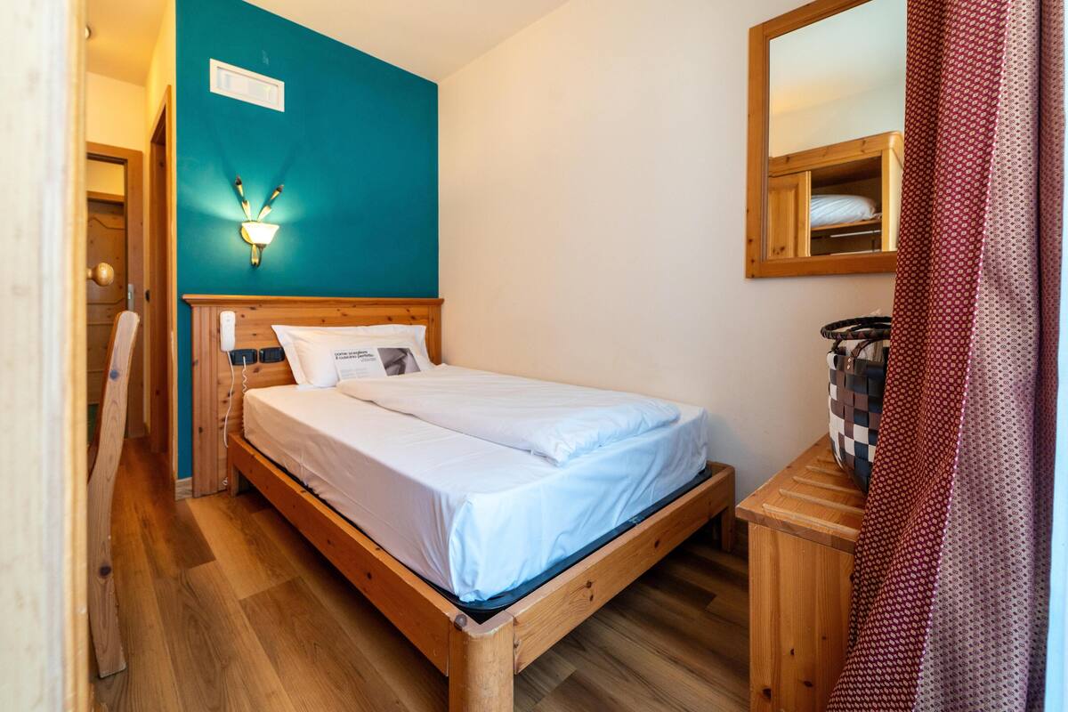 Un lit simple avec un cadre en bois, un mur d’accent de couleur turquoise et une petite table de chevet avec un panier.