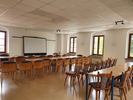Un salón de conferencias con mesas y sillas de madera, una pizarra y una pantalla para proyector.