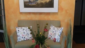 A cozy seating area with a sofa, a table with a book and flowers, and a framed painting on the wall. - Business Hotel Siebeneichen GmbH (Meissen)