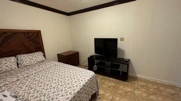 Un dormitorio con una cama, cabecera de madera, televisor sobre un mueble bajo y un armario pequeño.