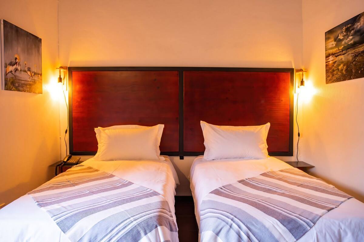 A hotel room with two beds, a wooden headboard, and wall-mounted lamps.
