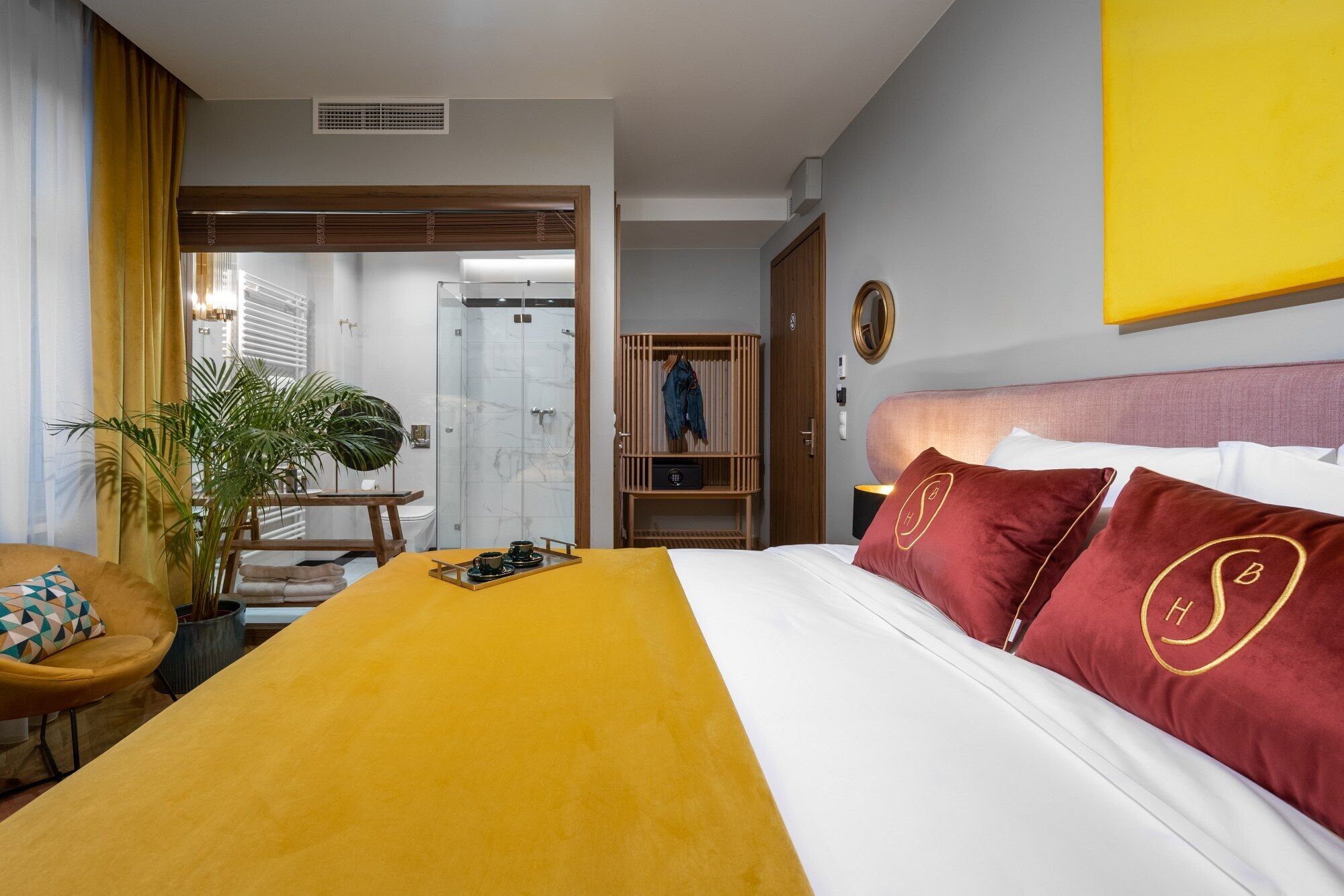Hotelkamer met een bed, een bureau, een stoel, een plant en een badkamer zichtbaar door een geopende deur.