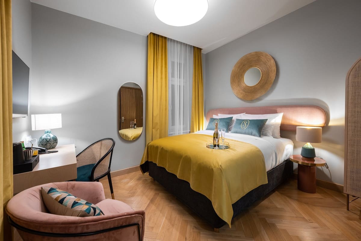 A modern hotel room with a bed, a desk, a chair, and a round mirror.