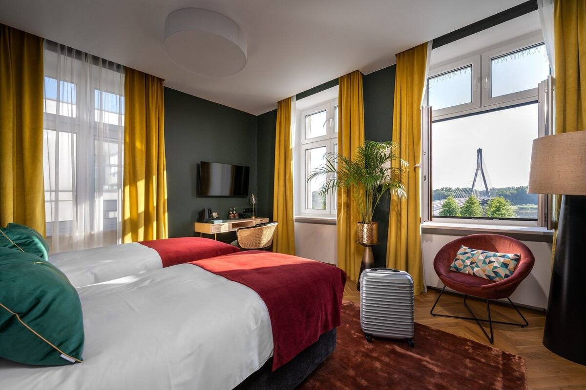 A hotel room with two beds, a desk, a chair, a TV, and a view of a bridge.