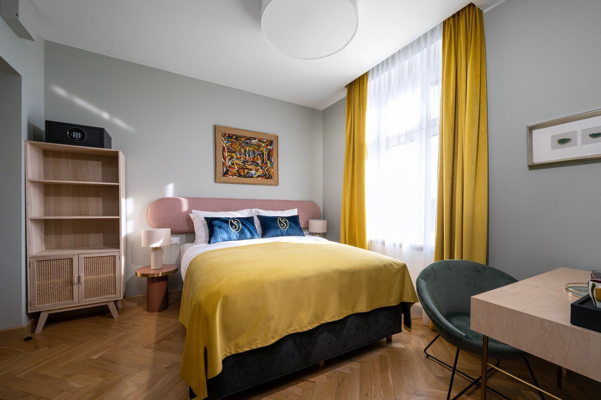 Une chambre d’hôtel avec un lit, un bureau, une chaise, une bibliothèque et un tableau au mur.