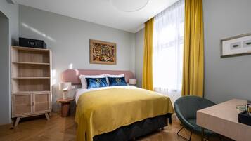 A hotel room with a bed, a desk, a chair, a bookshelf, and a painting on the wall.