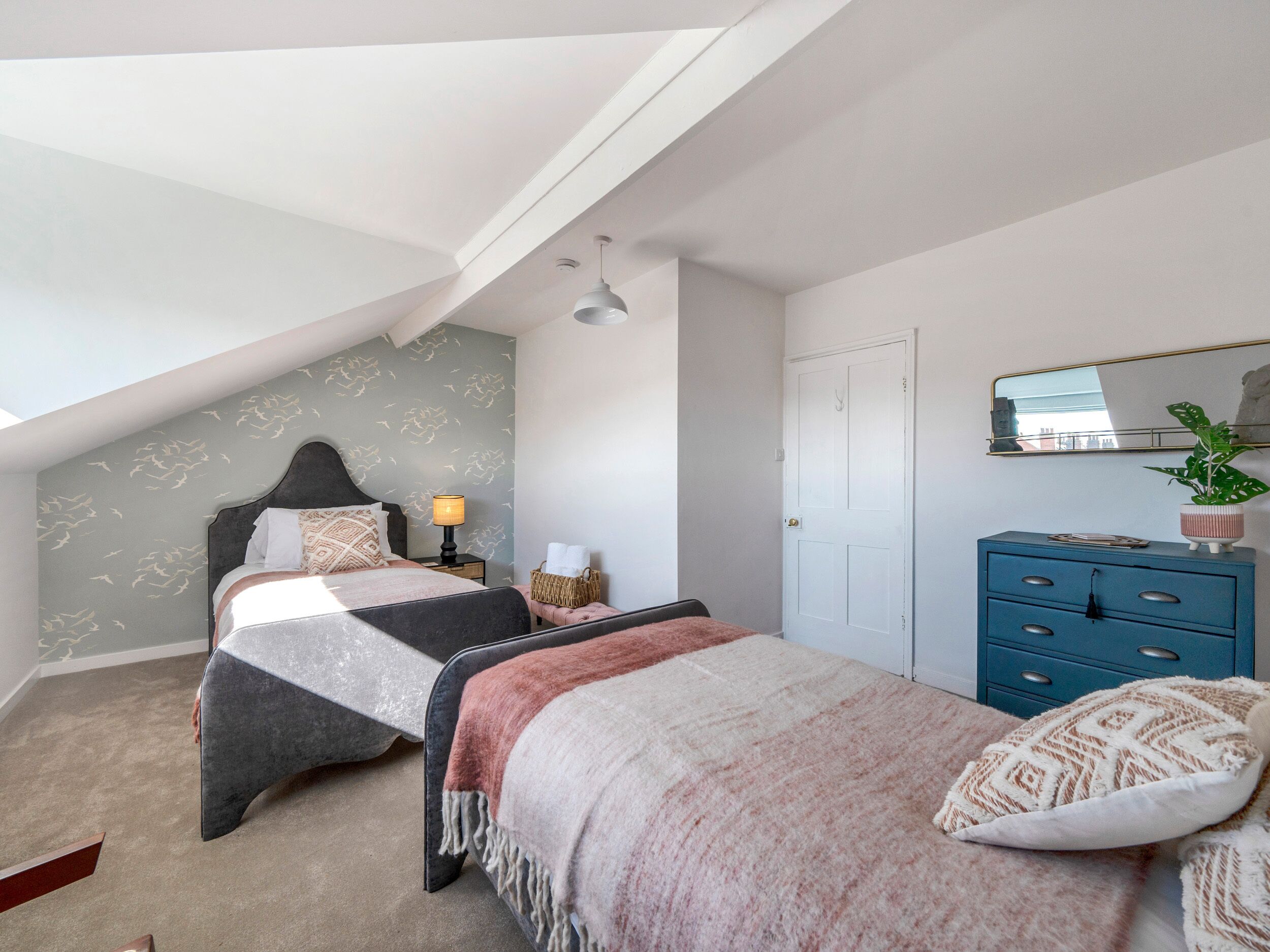 A bedroom with a sloped ceiling, a bed with a headboard, a dresser, a nightstand, a lamp, and a mirror.