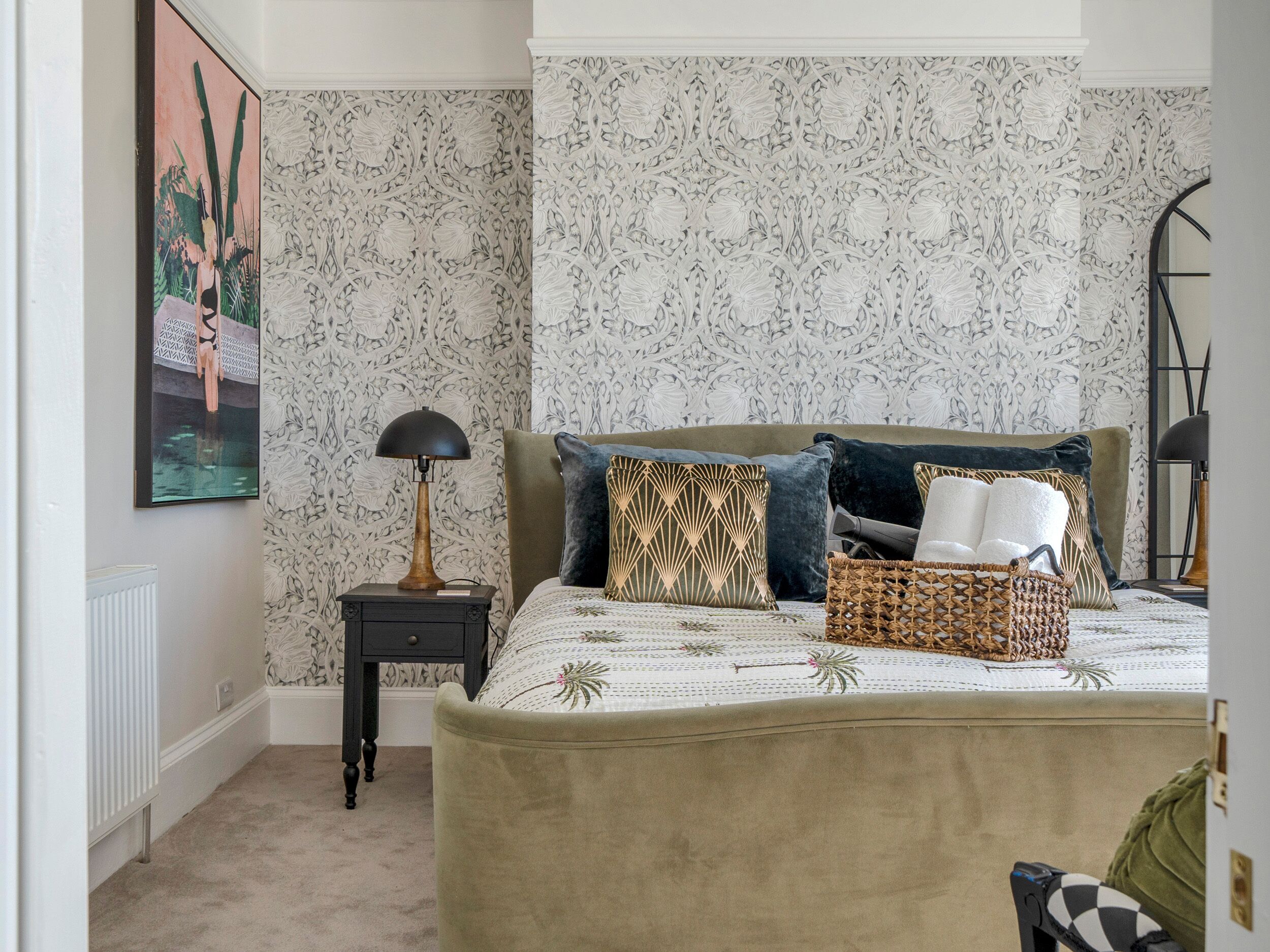 Een slaapkamer met een groot bed, een nachtkastje, een lamp en een decoratief wandobject.