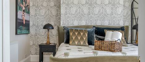 Een slaapkamer met een groot bed, een nachtkastje, een lamp en een decoratief wandobject.