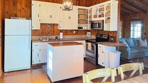 A rustic kitchen with wooden walls, white cabinets, a central island, and a dining area with a sofa and wooden chairs. - The Cozy Cabin on Lake Martin (Eclectic)