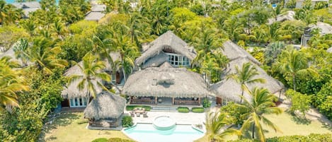 A resort with thatched-roof buildings, a swimming pool, and palm trees.