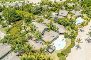 Luchtbeeld van een resort met villa's met rieten daken, een zwembad en weelderige tropische begroeiing.