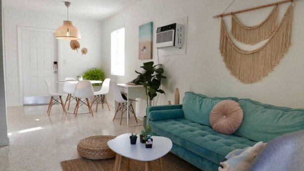 Una sala de estar moderna con un sofá color turquesa, una mesa de centro blanca y una zona de comedor con sillas blancas y una mesa de madera.