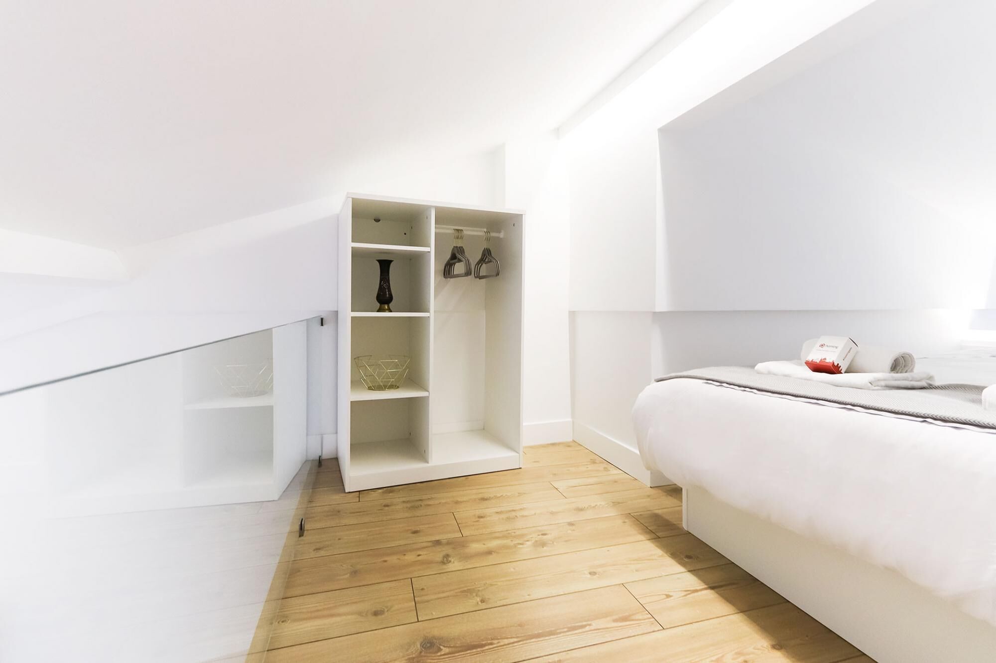 Une chambre moderne avec un plancher en bois, un lit blanc et une armoire intégrée dotée d’étagères.