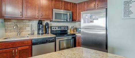 A kitchen with wooden cabinets, stainless steel appliances, granite countertops, and a dishwasher.