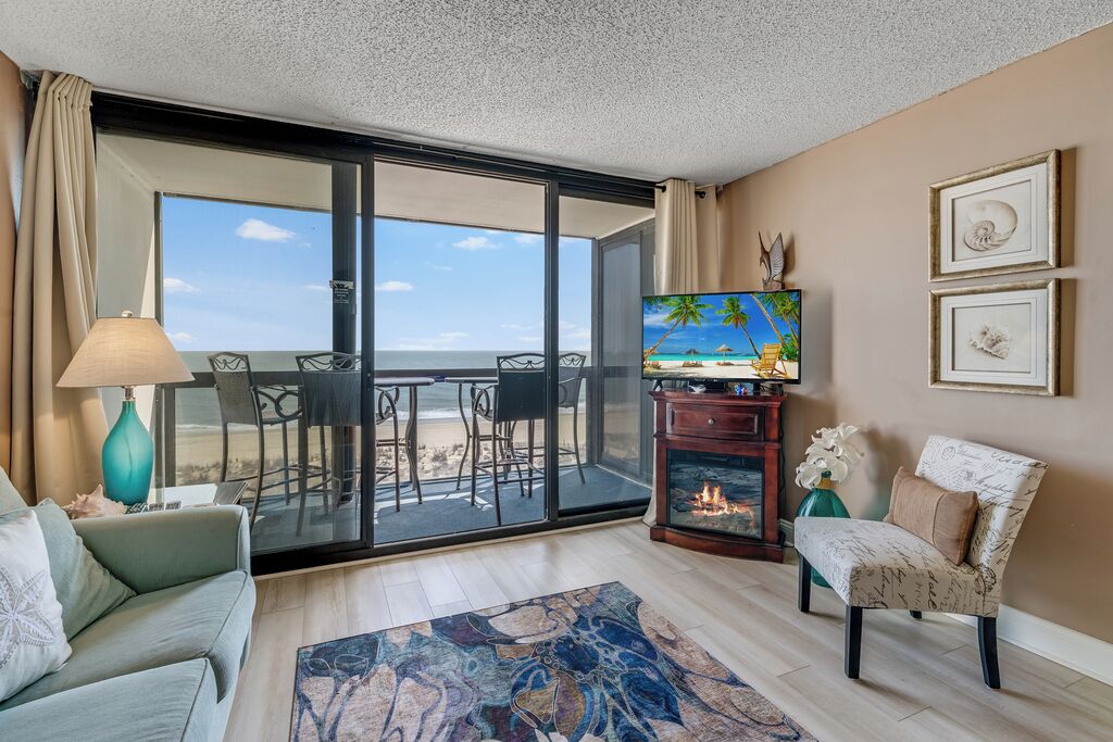 Un salon comprenant un canapé, un téléviseur, une cheminée et un balcon avec vue sur la plage.