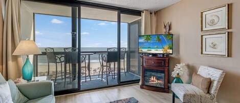 Un salon comprenant un canapé, un téléviseur, une cheminée et un balcon avec vue sur la plage.