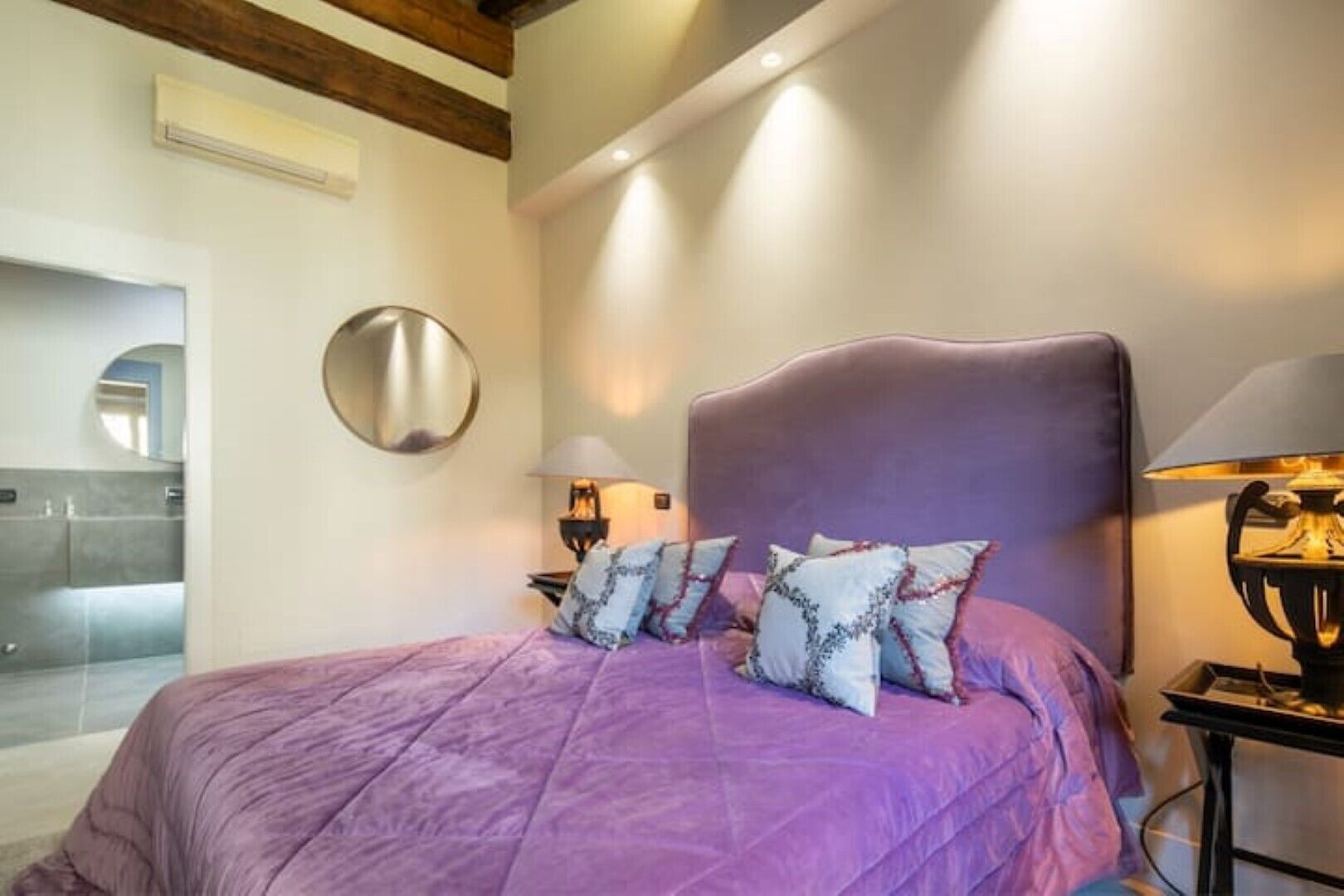 Une chambre à coucher avec un grand lit, une tête de lit, deux lampes de chevet et un miroir au mur.