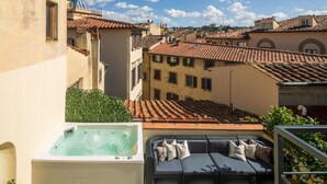Eine Dachterrasse mit Whirlpool, Sitzgelegenheiten im Freien und Blick auf eine historische Stadt mit Terrakotta-Dächern.