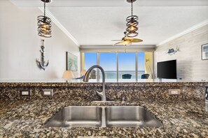 A kitchen with granite countertops, a double sink, pendant lights, and a ceiling fan.