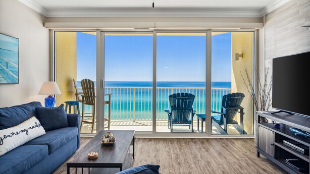 Ein Wohnzimmer mit einer Couch, Couchtisch und TV-Schrank, ein Balkon mit Stühlen und Meerblick.