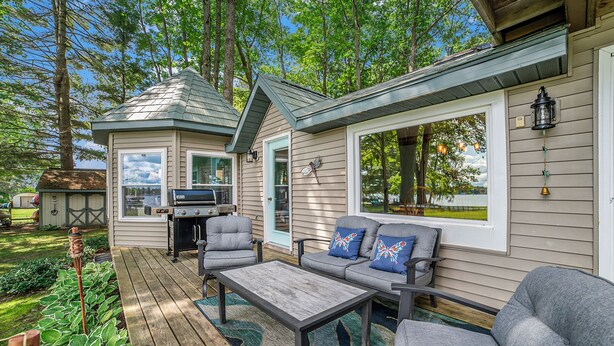 A deck with outdoor furniture, a grill, and a view of the surrounding trees. - Family Fun on Otsego Lake - HUGE yard, kayaks, paddleboards, zip line and more! (Gaylord)