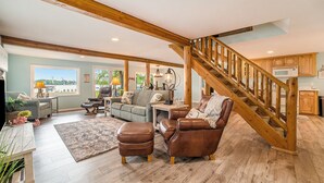 A spacious living room with a wooden staircase, a sofa set, and a view of the outdoors. - Family Fun on Otsego Lake - HUGE yard, kayaks, paddleboards, zip line and more! (Gaylord)