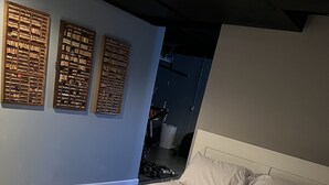 Un lit bien fait, avec une tête de lit et un pied de lit blancs, une grande fenêtre donnant sur l’extérieur et trois décorations murales en liège.