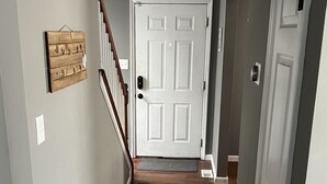 Un couloir doté d’un plancher en bois, d’un tapis rouge à motifs, d’une porte blanche et d’un escalier surmonté d’un luminaire.