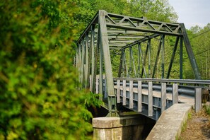 A steel truss bridge with a concrete base, surrounded by dense green foliage. - Riverside De Luxe*WiFi*Steps to the River (Elkins)