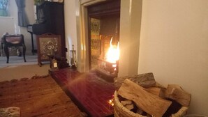A room with a fireplace, a woven basket with logs, a red rug, and a chair. - Peaceful Country Cottage (Kinghorn)