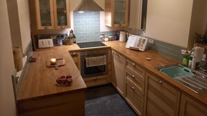 A compact kitchen with wooden cabinets, a black countertop, a built-in oven, and a sink with a dish rack. - Peaceful Country Cottage (Kinghorn)